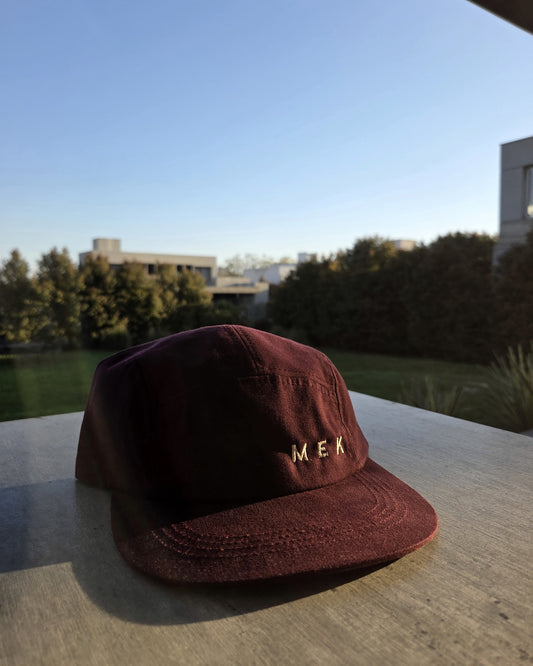 Gorra MEKap Five Panel bordó apoyada sobre una mesa de madera al atardecer